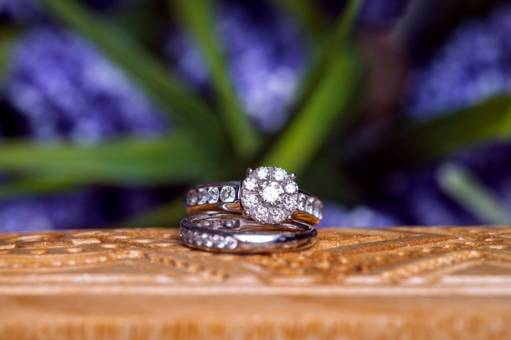 Close-up of diamond wedding rings on carved wood against a blurred floral background.